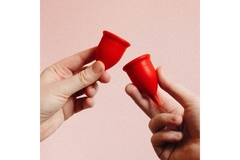 Image Two hands holding hot pink menstral cups in front of a pink background.